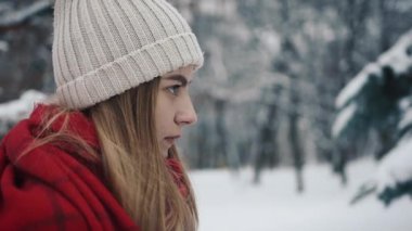 Noel ağaçları duran sıcak giysiler içindeki genç güzel kız ve ve bir akıllı telefon kullanır. Ağır çekim. Bir kış parkta şık genç güzel kız portresi