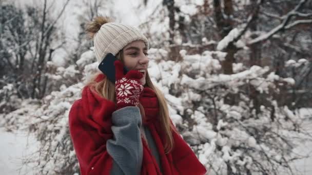 Ung vacker flicka i i varma kläder står nära de julgranar och talar via telefon. Slow motion. Porträtt av snygg ung vacker flicka i en winter park — Stockvideo