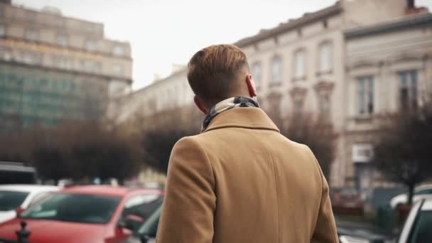 Um jovem homem de negócios com um manto a descer a rua com um tempo nublado. Movimento lento — Vídeo de Stock