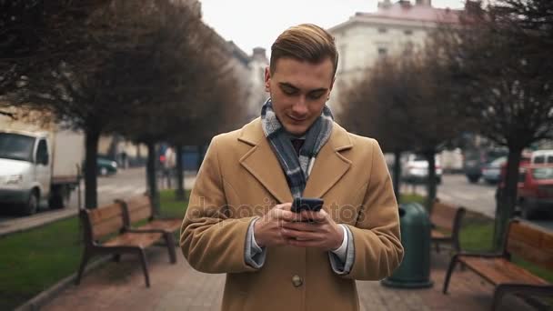 Joven hombre de negocios feliz usando el teléfono inteligente y caminando en la calle, cámara lenta — Vídeos de Stock