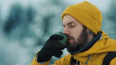 Güzel dağlar kış zamanında. Sarı kış giysileri giyen adam sakallı, sıcak çay veya kahve dışarıda soğukta içiyor