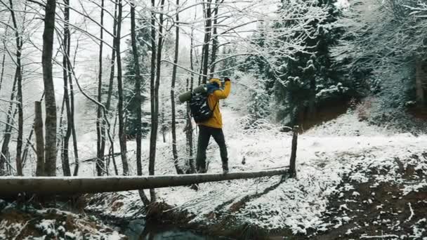 Snow-covered mountains during winter time. A hiker wearing a backpack is crossing the stream — Stock Video