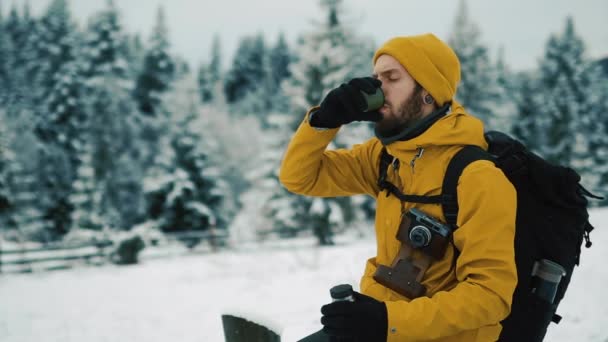 Prachtige bergen in de winter. Man met baard, gele winterkleren dragen is het drinken van hete thee of koffie buiten in de koude — Stockvideo