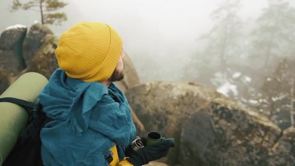 冬時間で美しい山々。黄色の冬の服を着て、髭男は、寒さの中熱いお茶やコーヒーを外を飲んでいます。スローモーション — ストック動画