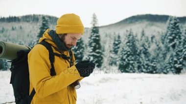 Sakal, bir telefonu kullanarak sarı kış giysileri giyen adam. Bir sırt çantası ile kış dağlarda bir uzun yürüyüşe çıkan kimse gider. Kış zamanında güzel dağlar