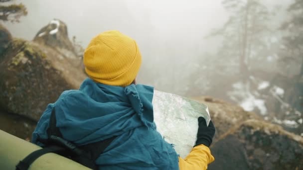 Mann mit Bart, in gelber Winterkleidung, hält die Landkarte in der Hand und prüft den Weg. Berge im Winter im Hintergrund — Stockvideo
