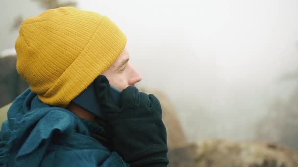 男人带着胡子, 穿着黄色的冬衣在电话里说话。一个徒步旅行者带着背包去冬天的山里。美丽的山在冬天时间 — 图库视频影像