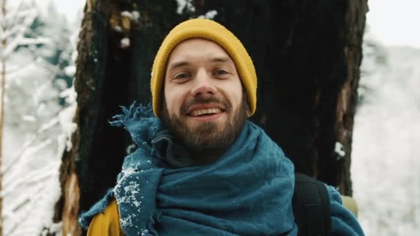 Portrait d'un homme vêtu d'hiver. Homme à la barbe, vêtu de vêtements d'hiver jaunes regarde la caméra et sourit. Vieil arbre en arrière-plan — Video