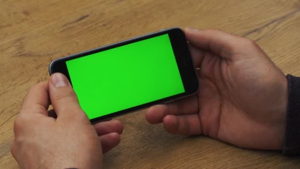 Человек с горизонтальным смартфоном с зеленым экраном. Крупный план рук человека с мобильным телефоном. Хрома-ключ. Закрывай. Горизонталь — стоковое видео
