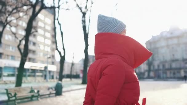 Mulher bonita em uma jaqueta vermelha fica na rua coberta de neve em um dia ensolarado de inverno — Vídeo de Stock