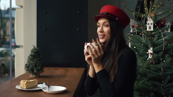 Encantadora mujer en sombrero rojo bebe café sentado en el acogedor café — Vídeo de stock