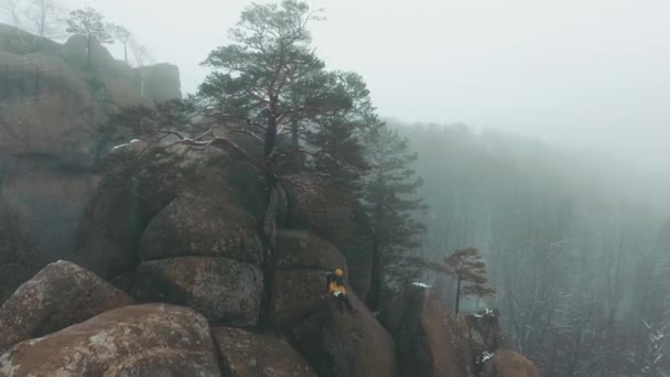 Air view at the man sitting on the top of the rock in winter mountains covered with fog — Stock Video