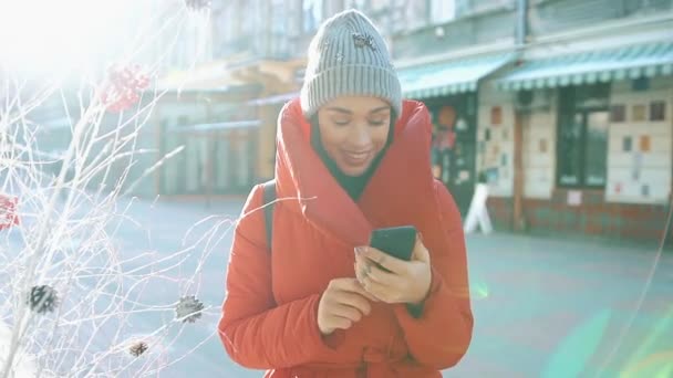 Mädchen in roter Winterjacke tippt etwas in ihr Handy, das auf der Winterstraße steht — Stockvideo