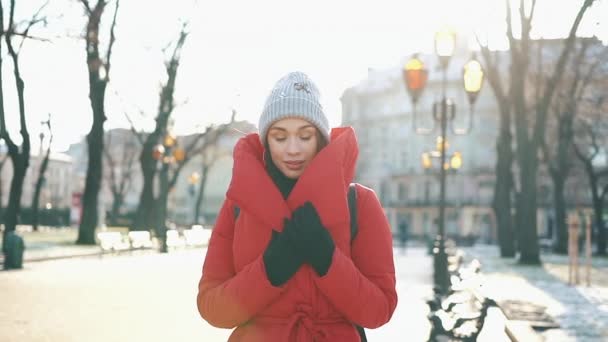 Vacker kvinna i en röd jacka står på gatan täckt med snö i en solig vinterdag — Stockvideo