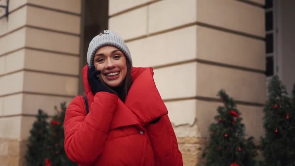 Hezká dívka v červené bundě rozhovory na smartphone stojící na ulici ve světlé zimní den — Stock video