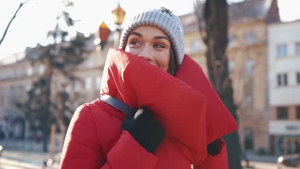 Belle femme dans une veste rouge se tient dans la rue couverte de neige dans une journée d'hiver ensoleillée — Video