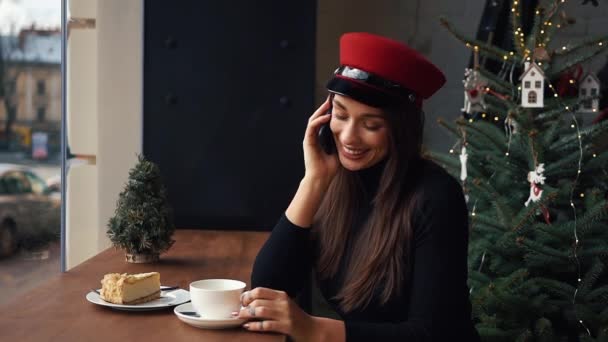 Mujer feliz habla por teléfono sentado en un acogedor café en frío día de invierno — Vídeos de Stock