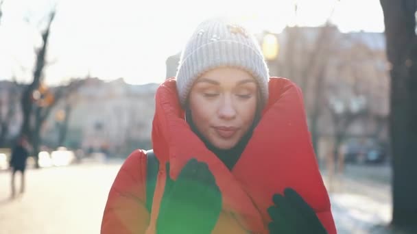 Mooie vrouw in een rood jasje staat op de straat die bedekt met sneeuw in een zonnige winterdag — Stockvideo