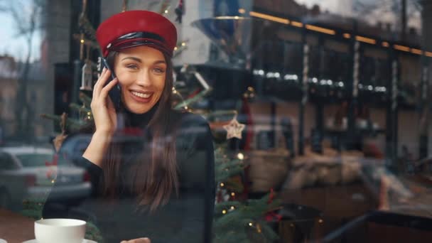 Mujer feliz habla por teléfono sentado en un acogedor café en frío día de invierno — Vídeos de Stock