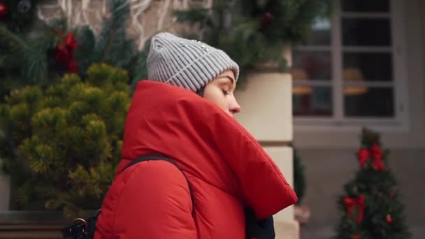 Hermosa mujer en chaqueta roja de invierno camina por la calle cubierta de nieve en una hermosa ciudad europea vieja — Vídeo de stock