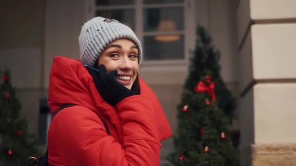 Chica bonita en chaqueta roja habla en el teléfono inteligente de pie en la calle en un día de invierno brillante — Vídeo de stock