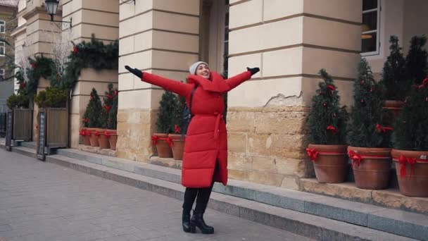Женщина в красной зимней куртке ходит по засыпанной снегом улице в красивом старом европейском городе — стоковое видео