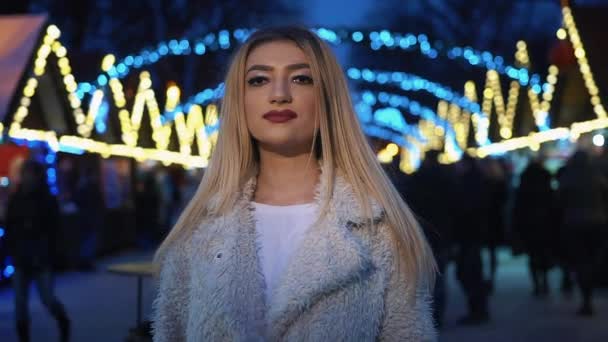 Αρκετά τρανσέξουαλ γυναίκα στέκεται στην πλατεία της πόλης μεταξύ των διακοσμήσεων Χριστουγέννων και κοιτάζει απευθείας στην κάμερα — Αρχείο Βίντεο