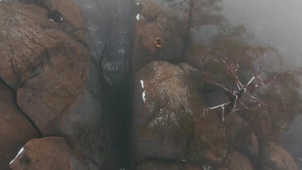 L'elicottero vola sopra le rocce dove l'uomo in giacca gialla sale attraverso la nebbia. Orario invernale — Video Stock