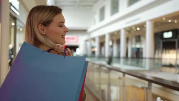 Van achteren kijken naar mooie vrouw lopen met een boodschappentas en wervelende rond in een winkelcentrum — Stockvideo