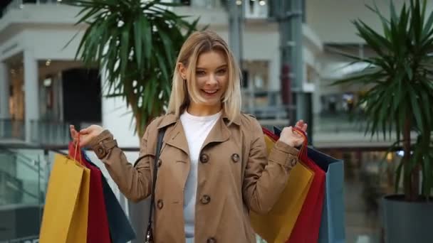 Laughing girl holds shopping bags on her shoulders standing in the mall — Stock Video