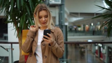 Kız onu telefon ayakta alışveriş torbaları ile alışveriş merkezinde omzuna denetler