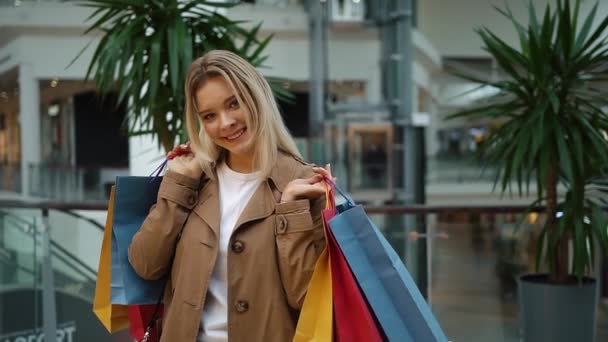Laughing girl holds shopping bags on her shoulders standing in the mall — Stock Video