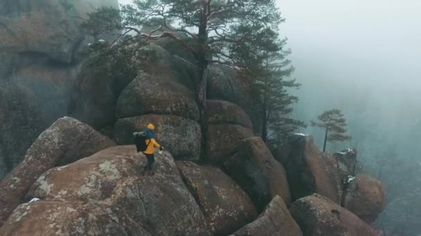 Mann in gelber Jacke erklimmt nebelverhangene Felsen — Stockvideo