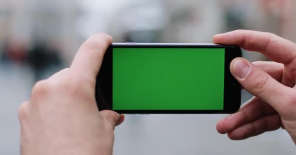 Чоловік тримає смартфон із зеленим екраном на руках, стоячи на вулиці — стокове відео