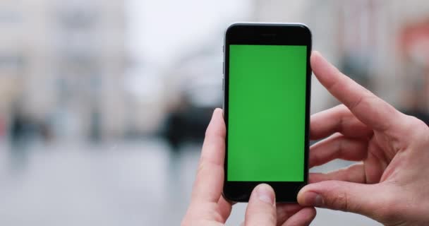 Man håller en smartphone med grön skärm i famnen stående på gatan — Stockvideo