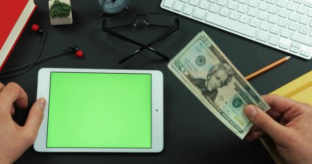 Человек держит в руке сотни долларов, а потом печатает что-то на зеленом экране планшета. — стоковое видео