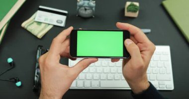 Adam yeşil ekran siyah bir smartphone bir çalışma tablosu üzerinde tutar.