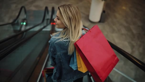 Jovem loira de jeans jaqueta vai para baixo nas escadas em movimento no shopping — Vídeo de Stock