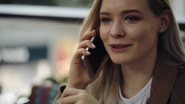 Charmant blond meisje gesprekken over de smartphone zitten in Cafe — Stockvideo