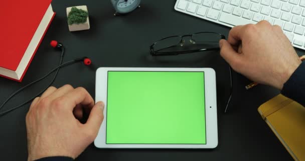 Человек кладет свои очки на планшет с зеленым экраном на стол и масштабирует экран — стоковое видео