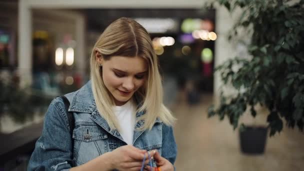 Chica mira dentro de sus bolsas de compras de pie en el centro comercial — Vídeos de Stock