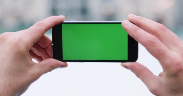 Snow falls over a mans hand holding smartphone with green screen in his arm and taps something on it — Stock Video