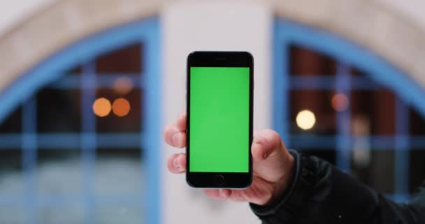 Neve cai sobre um homem mão segurando smartphone com tela verde em seu braço — Vídeo de Stock