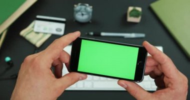 Adam yeşil ekran ile smartphone bir çalışma tablo üzerinde tutar.