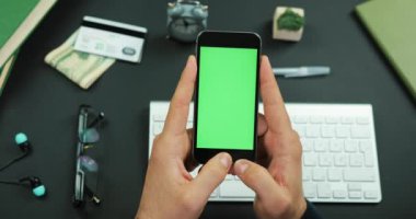 Adam yeşil ekran siyah bir smartphone bir çalışma tablosu üzerinde tutar.