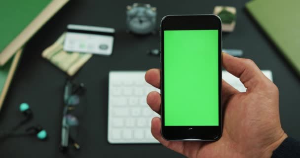 El hombre sostiene el teléfono inteligente con pantalla verde sobre una mesa de trabajo — Vídeos de Stock