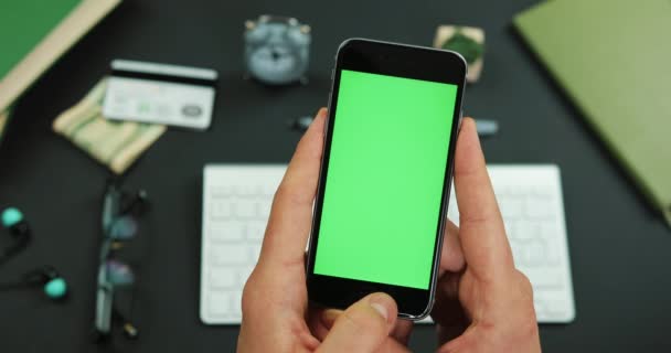 Mannen innehar smartphone med grön skärm över ett arbetsbord och kranar något på det — Stockvideo
