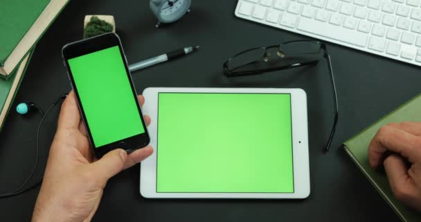 Homem segura smartphone com tela verde sobre uma mesa com tela verde e toca em algo nele — Vídeo de Stock