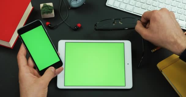 Homem segura smartphone com tela verde sobre uma mesa com tela verde e coloca seus óculos na mesa — Vídeo de Stock