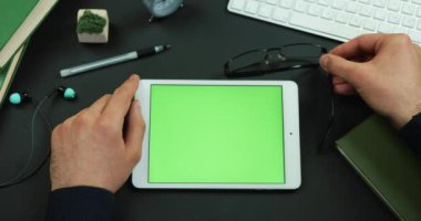 Tablet yeşil ekran ile çalışma tablosu üzerinde yatıyor ve erkek gözlük arkasında koyar